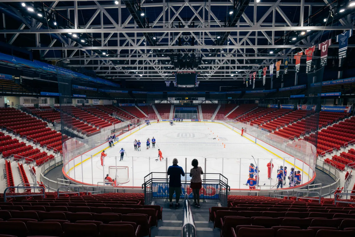 A man and woman look out to a hockey rink with players on the ice. 